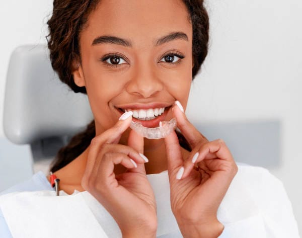 Person holding clear aligners, smiling warmly in a dental office setting, showcases the confidence that comes with expert care from an orthodontist.
