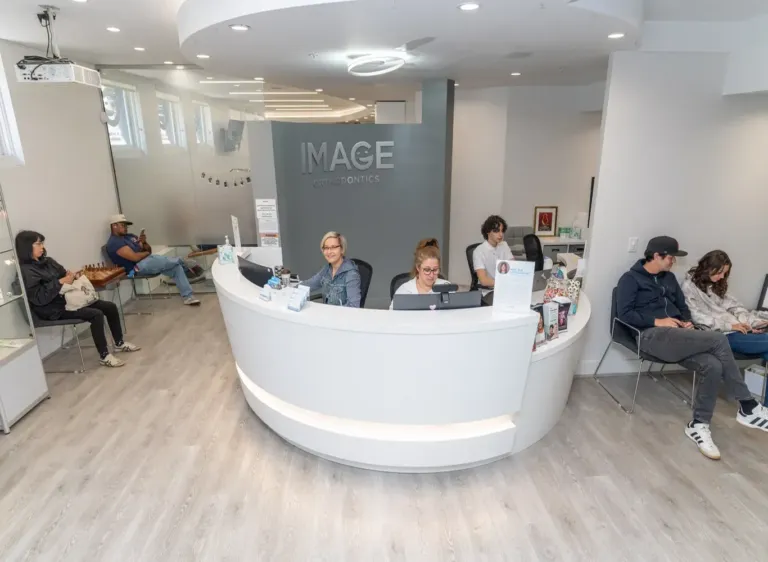 Two staff members work at the Image Orthodontics reception desk, with patients waiting nearby for treatments including clear aligners and braces.