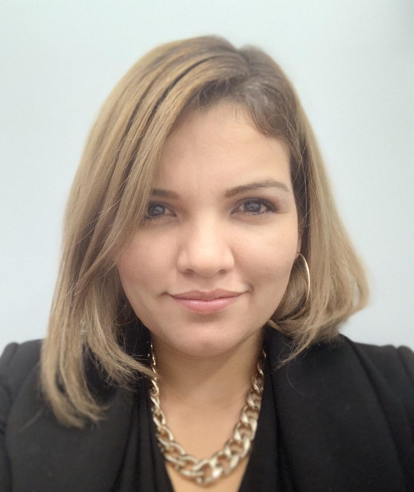 A professional headshot of a Pleasanton orthodontist with shoulder-length hair, wearing a black top and a gold chain necklace.