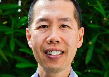 Dr. Benson Wong, B.S., DDS. A person with short hair smiles confidently, perhaps after a visit to their South San Francisco orthodontist, in front of vibrant green foliage.