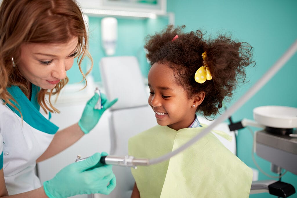preventative orthodontic care at Image Orthodontics Female dental professional wearing gloves shows a young girl a dental tool during a checkup.