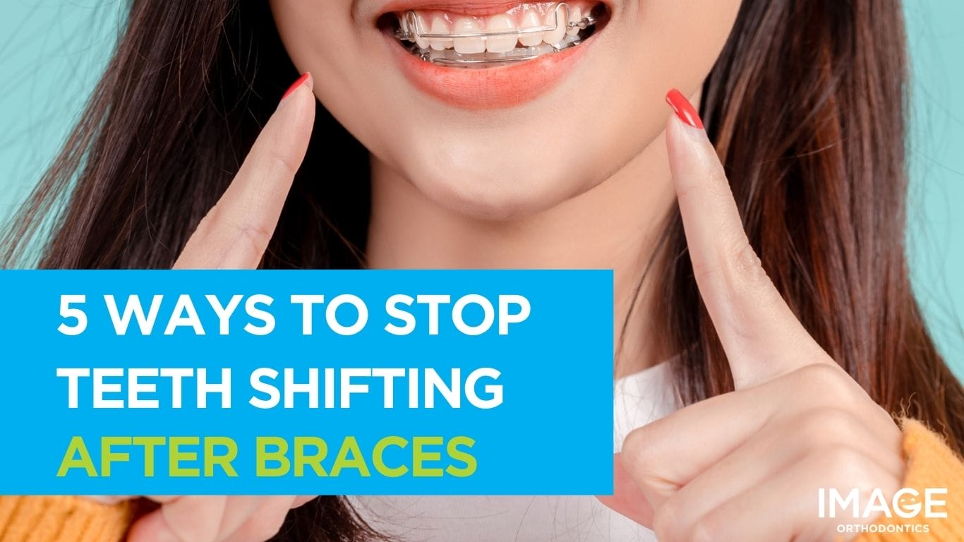 A smiling young woman pointing to her teeth while wearing a clear orthodontic retainer