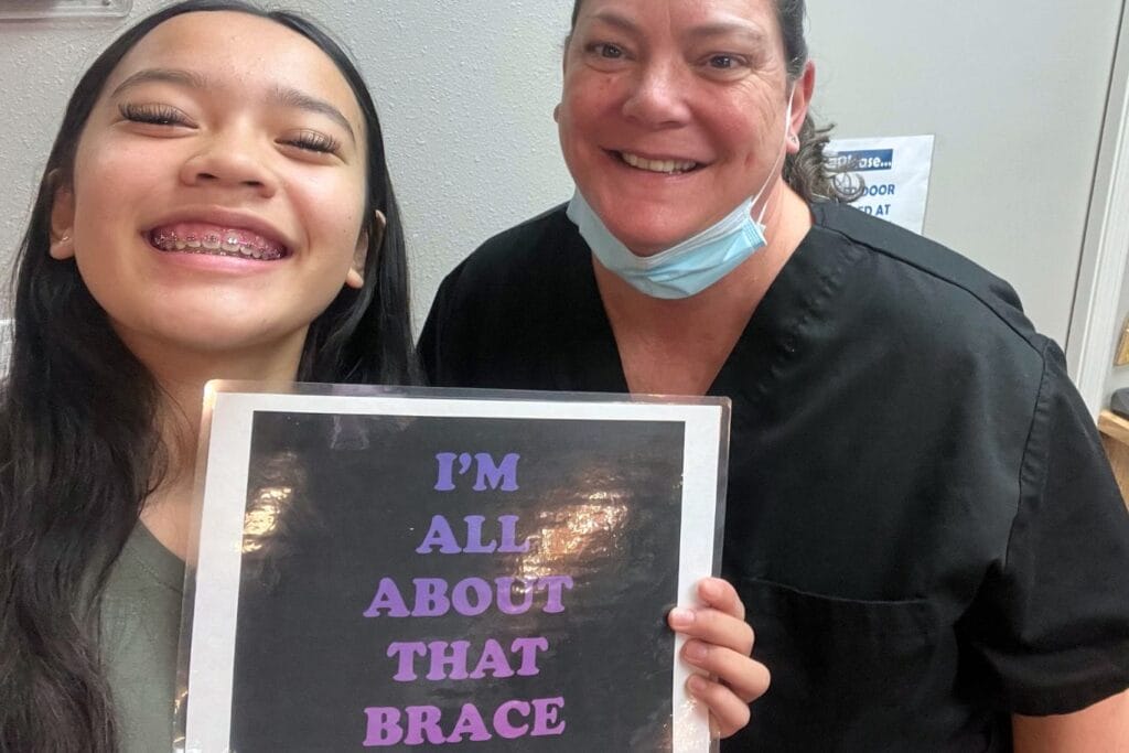 Smiling teen patient wearing braces poses with an Image Orthodontics team member at the ends of treatment, holding a sign celebrating braces and successful orthodontic care.