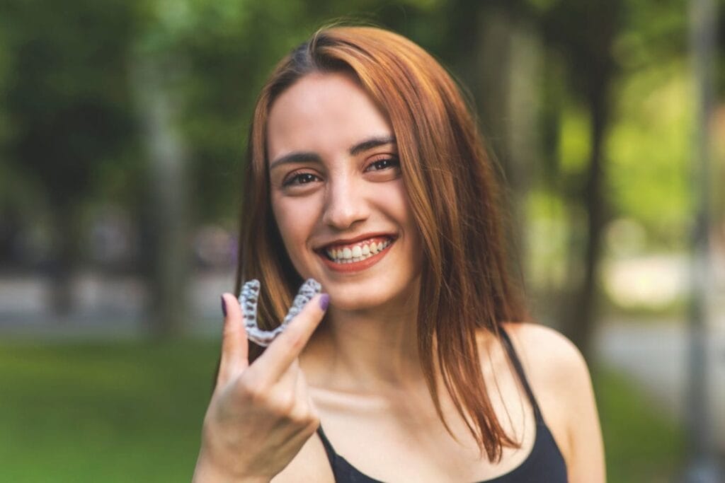 Smiling young woman holding clear Invisalign aligners outdoors