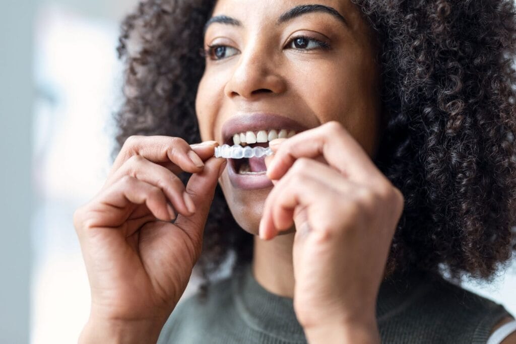 Close-up of a woman placing clear aligners on her teeth, an orthodontic option suitable for musicians.