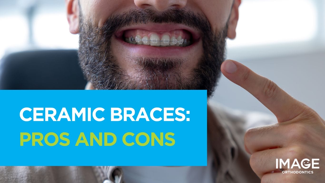 Close-up of a bearded man smiling and pointing to his ceramic braces on his teeth.