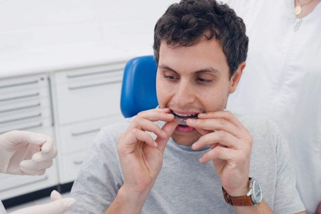 Learn the invisalign process at Image Orthodontics. Man sitting in a dental chair placing clear aligners on his teeth during an Invisalign fitting.