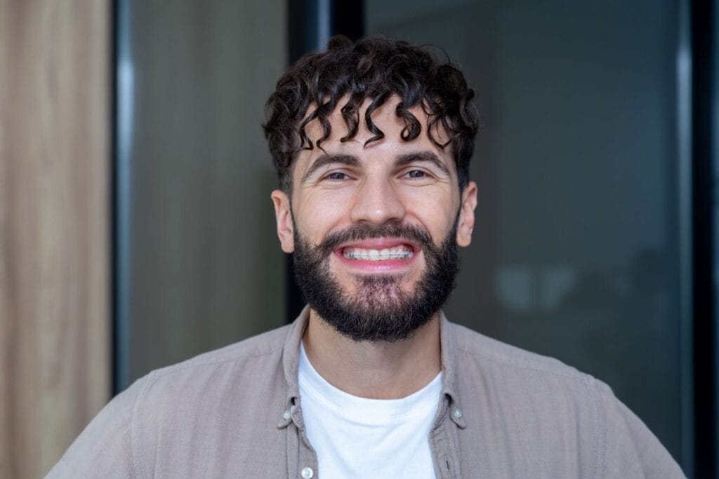 Smiling bearded man with curly hair wearing ceramic braces