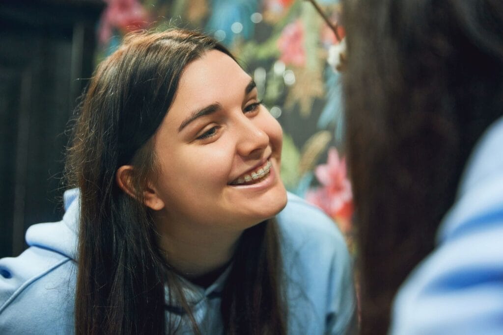 Smiling young woman wearing ceramic braces, looking at her reflection in a mirror
