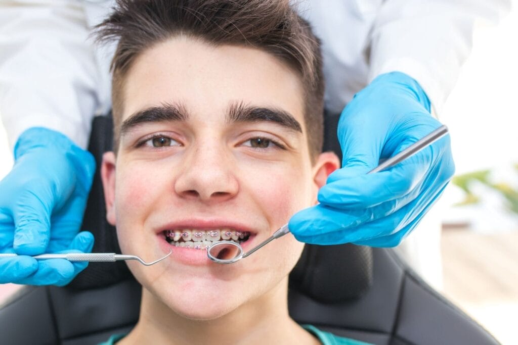 Teenage boy with braces sitting in a dental chair while a clinician examines his teeth, with braces helping correct jaw misalignment